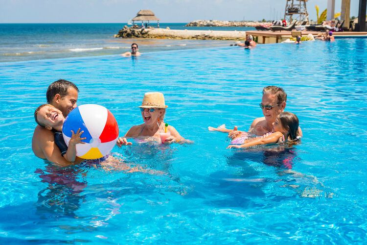Gente jugando en la piscina con pelota, océano al fondo