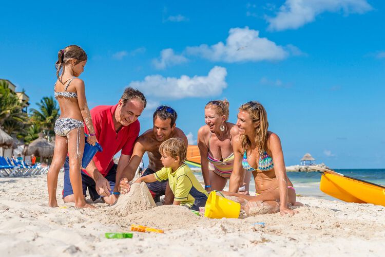 Una familia haciendo formas de arena con niños en la playa.