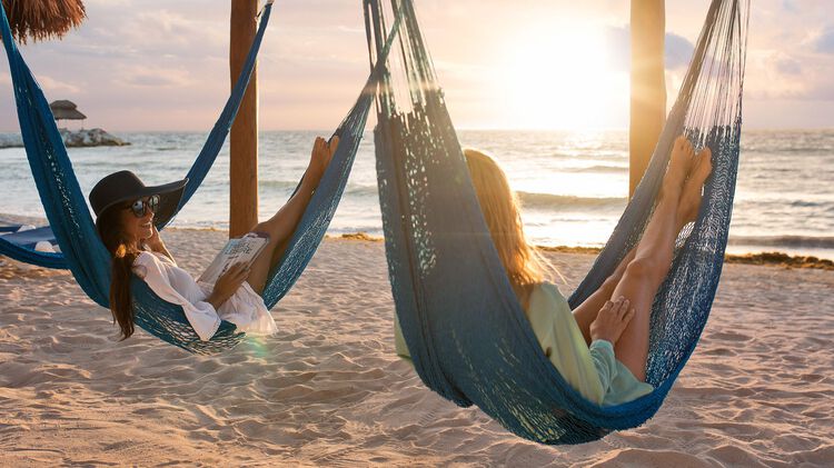 Two women in hammock swings on beach with sunset view on the ocean