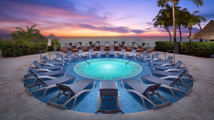Jacuzzi surrounded by pool chairs with sunset ocean view in the background